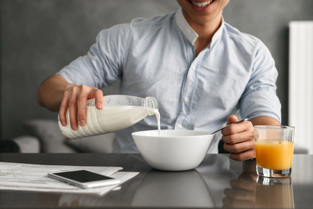 Close u[p of a smiling young asian man having breakfast while sitting at the table on a kitchen at homeの写真素材
