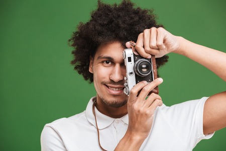 Picture of happy young african curly man photographer isolated over green wall background holding...