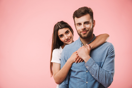 Portrait of a smiling young couple hugging while standing isolated over pink backgroundの写真素材