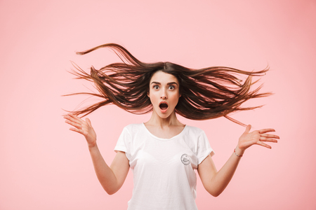 Portrait of a shocked young woman with long hair jumping isolated over pink backgroundの写真素材
