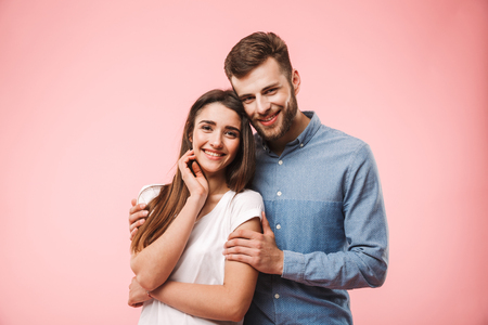 Portrait of a beautiful young couple hugging while standing isolated over pink backgroundの写真素材