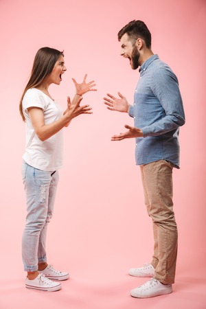 Full length portrait of a mad young couple having an argument isolated over pink backgroundの写真素材