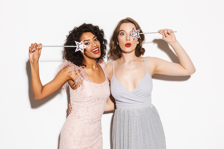 Portrait of two happy well dressed women having fun with magical wands isolated over white backgroundの写真素材