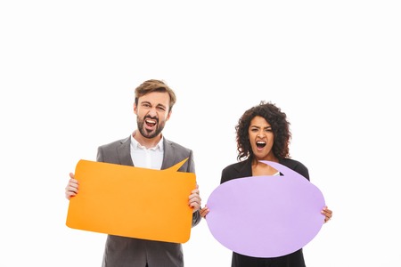Portrait of a furious young business couple holding empty speech bubbles isolated over white...