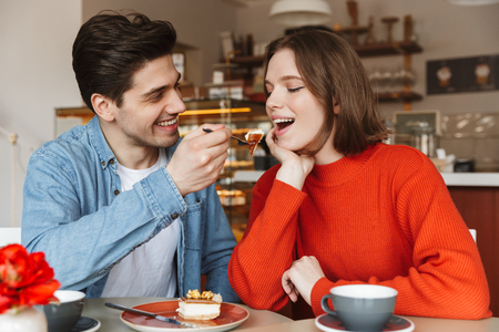 Portrait of happy couple dating, while man feeding girl with tasty cake in cozy bakeryの写真素材