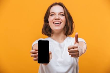 Image of excited young woman standing isolated over yellow background showing display of by mobile...
