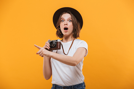 Image of excited emotional young woman photographer tourist standing isolated over yellow background holding camera pointing.の写真素材
