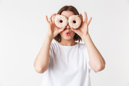 Portrait of a smiling young woman holding two donuts at her face isolated over white backgroundの写真素材
