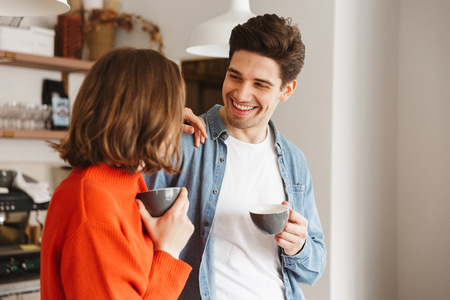 Caucasian people woman and man in casual wear smiling to each other and drinking coffee in cafeの写真素材