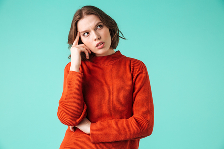 Portrait of a thoughtful young woman dressed in sweater looking away at copy space isolated over blue backgroundの写真素材