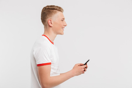 Profile image of satisfied teenage man wearing casual clothing typing and browsing internet on cell...