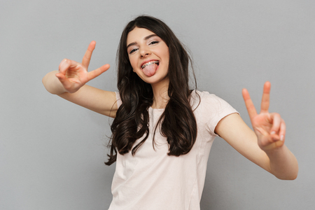 Photo of pretty cute young lady standing isolated over grey background wall showing peace gesture.の写真素材