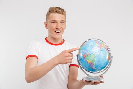 Portrait of a pensive teenage boy pointing at a globe isolated over white backgroundの写真素材