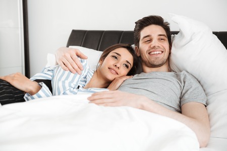 Portrait of a smiling young couple lying together in bedの写真素材