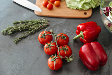 Close up of a kitchen table with tomtoes, capsicum and chopping boardの写真素材