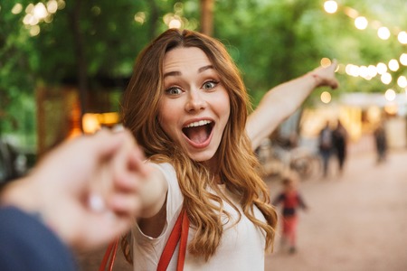 Close up of excited young girl pointing away while standing at the park and holding men's handの写真素材
