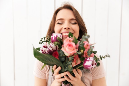 Young cute happy florist woman standing with flowers in workshop.