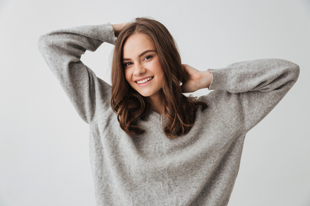 Happy brunette woman in sweater posing and looking at the camera over grey backgroundの写真素材