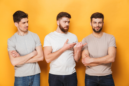 Two young upset men looking at their male friend isolated over yellow backgroundの写真素材