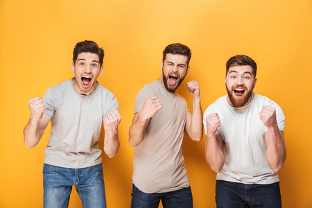 Three young excited men celebrating success together isolated over yellow backgroundの写真素材