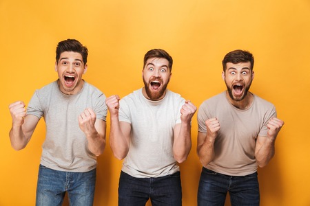Three young happy men celebrating success together isolated over yellow backgroundの写真素材