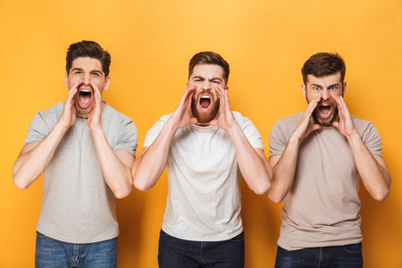 Three young angry men shouting isolated over yellow backgroundの写真素材
