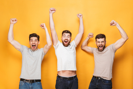 Three young excited men celebrating success and screaming isolated over yellow backgroundの写真素材