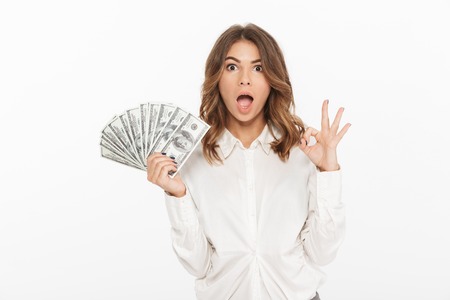 Portrait of an excited young business woman holding money banknotes isolated over white backgroundの写真素材