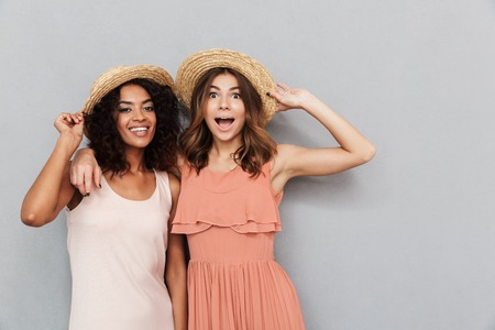 Portrait of two smiling young women dressed in summer clothes looking at camera isolated over gray backgroundの写真素材
