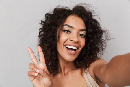 Close up portrait of a happy young african woman taking a selfie with outstretched arm over gray backgroundの写真素材