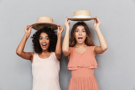 Portrait of two cheerful young women dressed in summer clothes looking at camera isolated over gray backgroundの写真素材