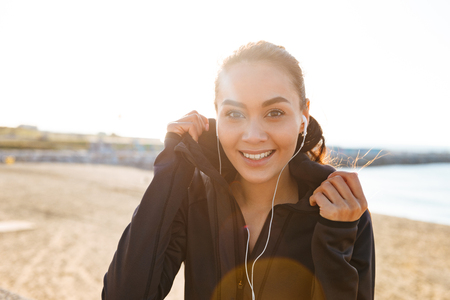 Photo of cheerful young asian sports woman sitting outdoors listening music looking camera.の写真素材