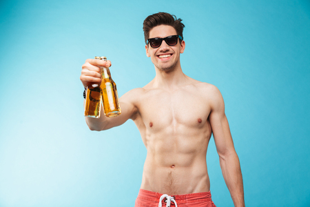 Portrait if a smiling shirtless man showing beer bottle over blue backgroundの写真素材
