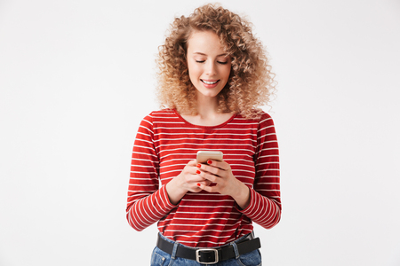 Portrait of happy young girl with curly hair holding mobile phone isolated over white backgroundの写真素材