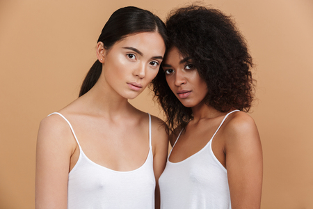 Two mystery women posing together and looking at the camera over beige backgroundの写真素材