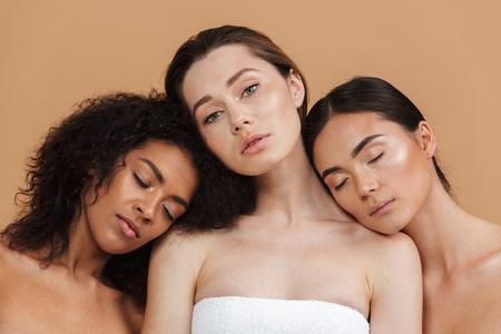 Beauty portrait of three nude multiracial women: caucasian, african american and asian girls posing together isolated over beige backgroundの写真素材