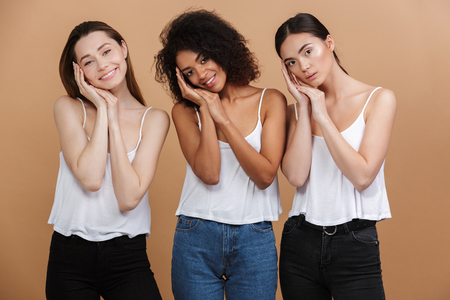 Three happy pretty women posing together and looking at the camera over beige backgroundの写真素材