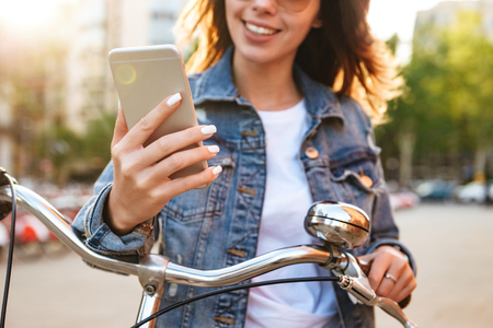 Cropped image of young beautiful lady outdoors on bicycle on the street using mobile phone.の写真素材