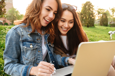 Image of two young beautiful happy women friends outdoors using laptop computer in park.の写真素材