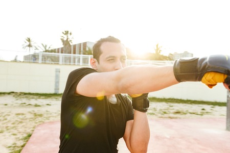 Image of young concentrated strong sports man boxer outdoors make exercises in gloves.