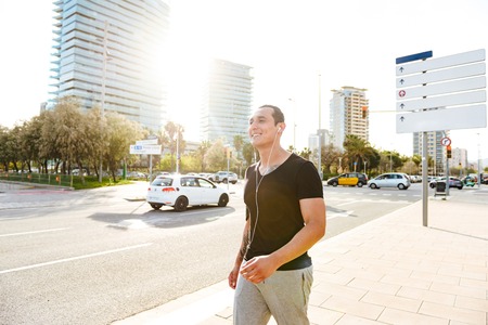 Image of handsome young strong sports man outdoors running listening music.