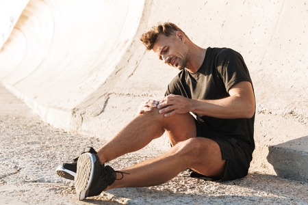 Portrait of an injured sportsman suffering from knee pain while sitting outdoorsの写真素材