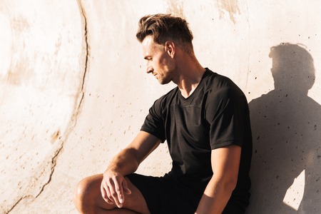 Portrait of a fit sportsman leaning on a wall while sitting outdoorsの写真素材