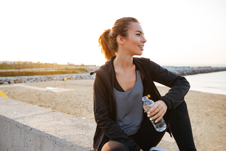 Image of happy beautiful young sports woman drinking water outdoors on the street.の写真素材