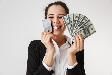 Photo of excited happy young business woman with credit card and money isolated over white wall backgound.の写真素材