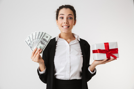 Photo of excited emotional young business woman holding surprise gift present box and money isolated over white wall backgound.の写真素材