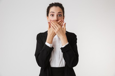 Portrait of a shocked young businesswoman covering mouth with armsm isolated over white backgroundの写真素材