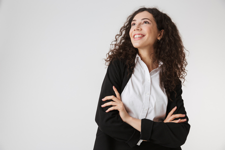 Portrait of a happy young businesswoman standing with arms folded and looking at copy space isolated over white backgroundの写真素材