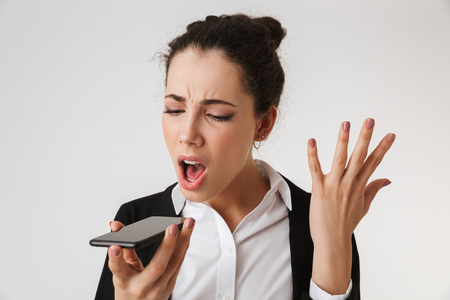 Image of young emotional screaming business woman isolated over white wall backgound looking aside talking by phone.の写真素材