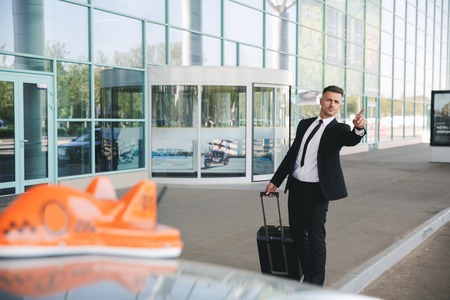 Serious businessman walking outside the airport with a suitcase and catching taxiの写真素材